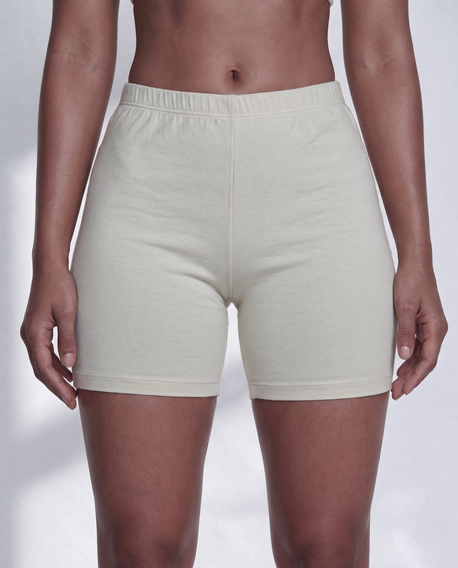 Woman relaxing in bed wearing soft undyed organic cotton boy shorts and a light sleep top